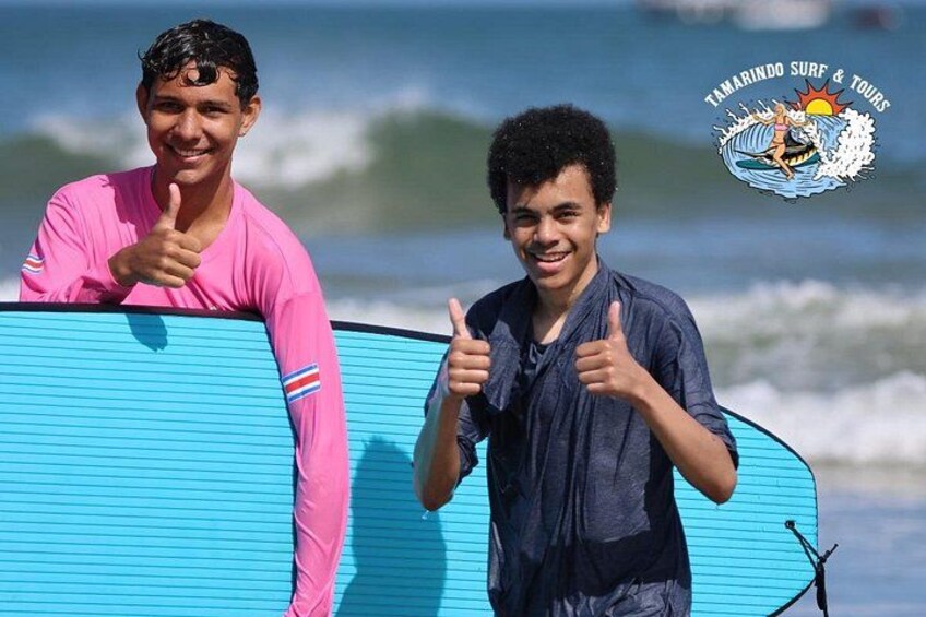 Two people holding surfboards on a beach with ocean waves in the background. 1