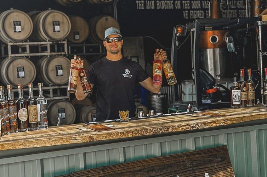 A bartender holding bottles of liquor behind a bar with various bottles and a sign in the background. 2