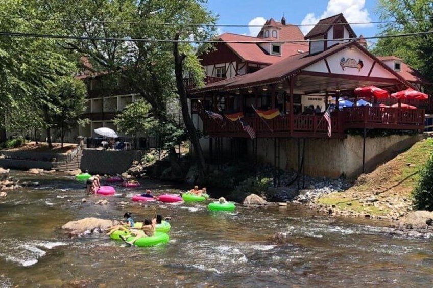 Ein Fluss, auf dem Menschen mit Luftmatratzen treiben, ein Gebäude mit rotem Dach und Bäume im Hintergrund. 2