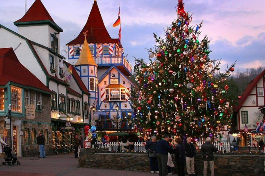 Un árbol de Navidad adornado con adornos y luces, rodeado de edificios tradicionales europeos con tejados rojos. 1