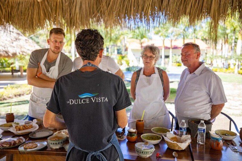 Un grupo de personas alrededor de una mesa con comida y bebidas, bajo un techo de paja. 1