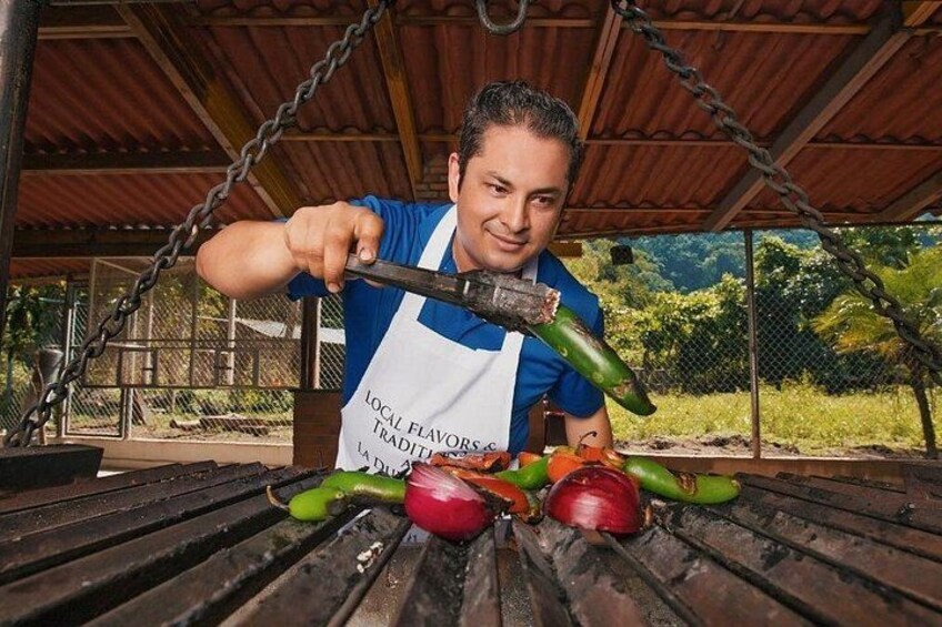 Una persona asando verduras bajo un techo, con una cerca de malla metálica al fondo. 2