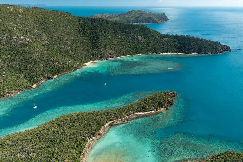 A coastal landscape with clear turquoise waters, a small island, and a distant mountain range. 3