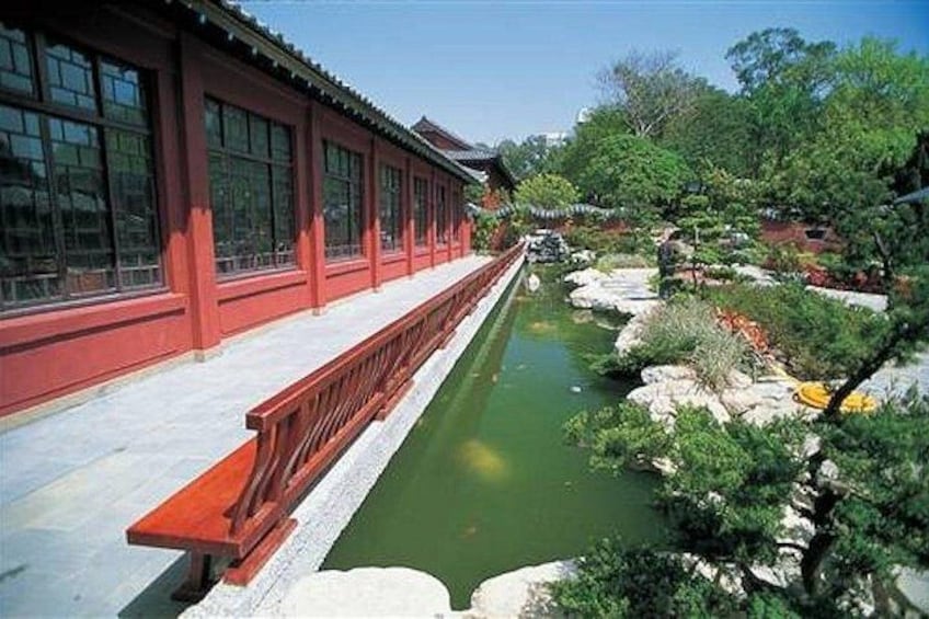 A traditional red building with a long corridor and a small pond with rocks and greenery. 3
