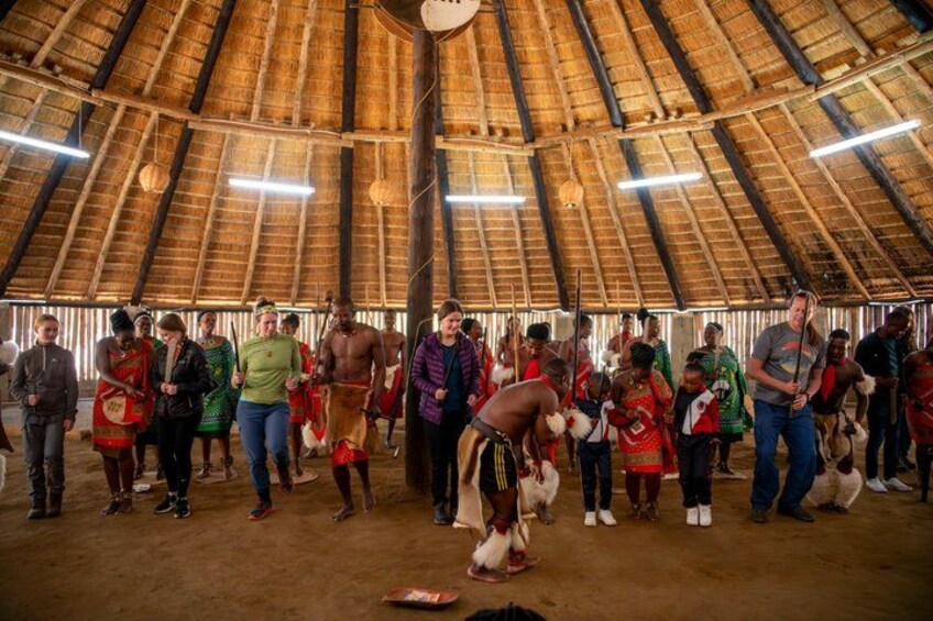 A group of people inside a thatched-roof structure, some holding musical instruments. 3