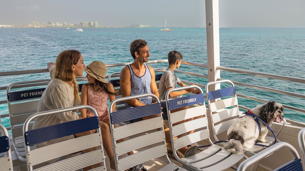 People on a boat with a dog, water, and a city skyline in the background. 1
