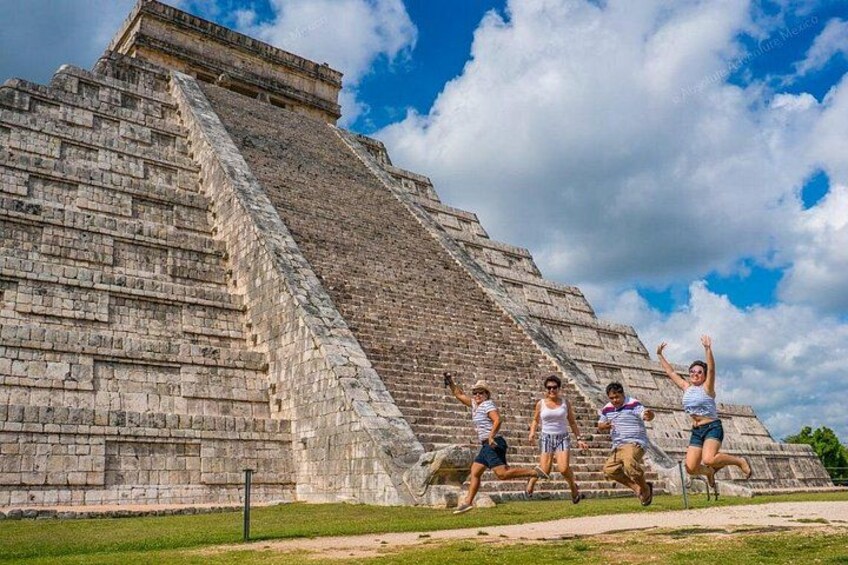 A large ancient pyramid with people jumping in front of it. 1