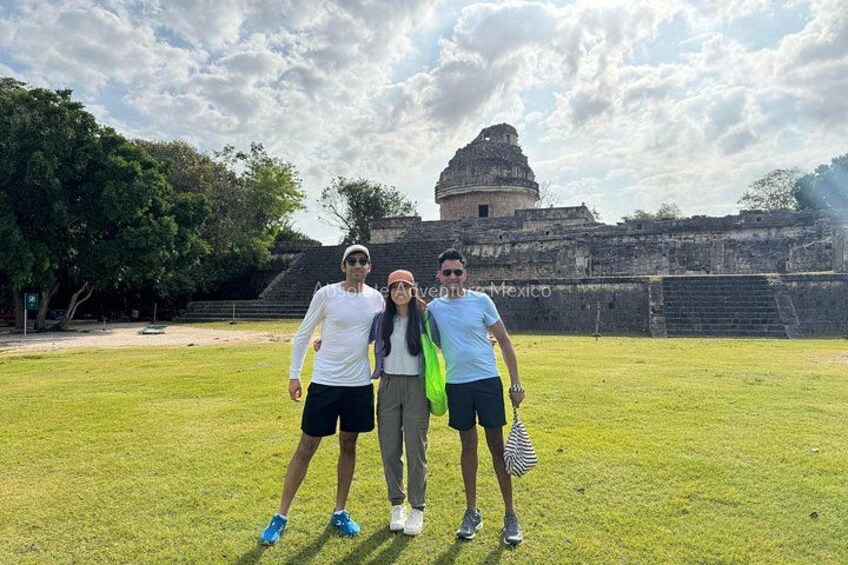 Three people standing in a grassy area with a historical structure in the background. 4