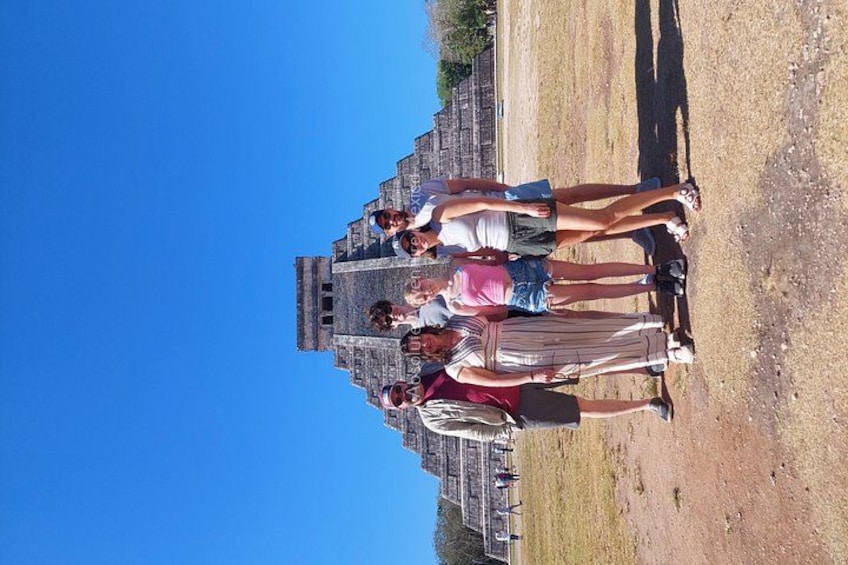 A group of people standing in front of a large, ancient stone structure with a clear blue sky in the background. 2