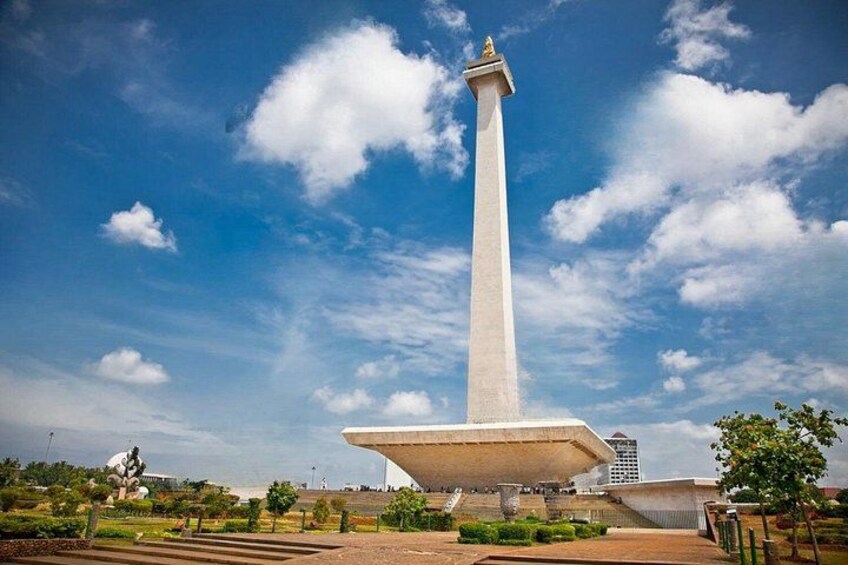 Un monumento alto y blanco con una base ancha, rodeado de un área ajardinada con árboles y un cielo azul despejado. 3