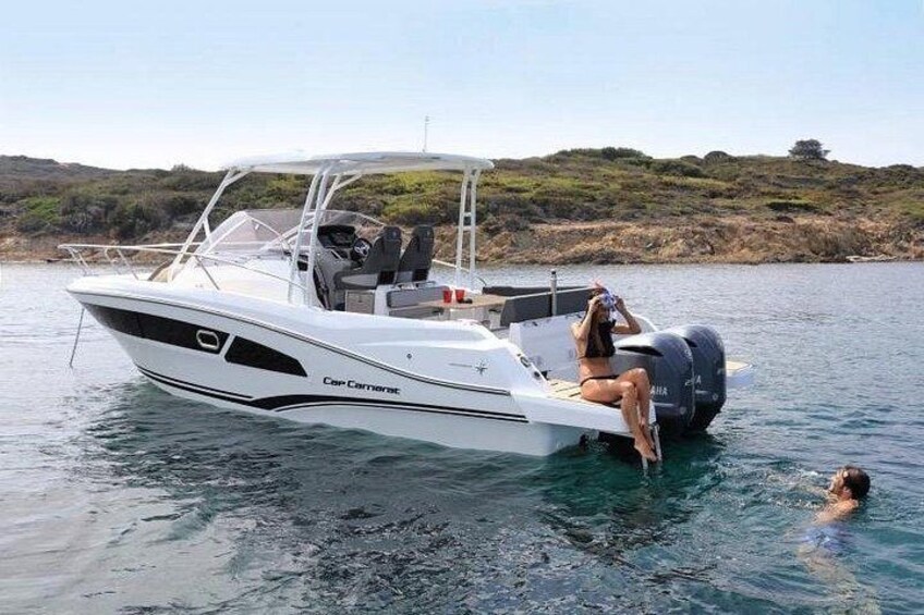 Un bateau à moteur blanc, baptisé Cap Camaret, navigue sur une eau calme. Une personne est assise au poste de pilotage et une autre personne nage à proximité. 1