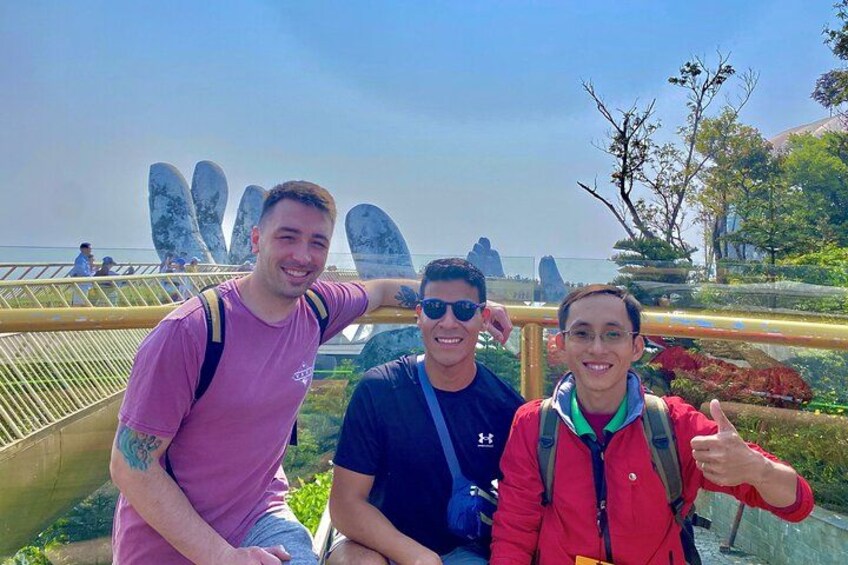 Three people sitting on a bridge with a scenic view of a park and a large sculpture in the background. 2