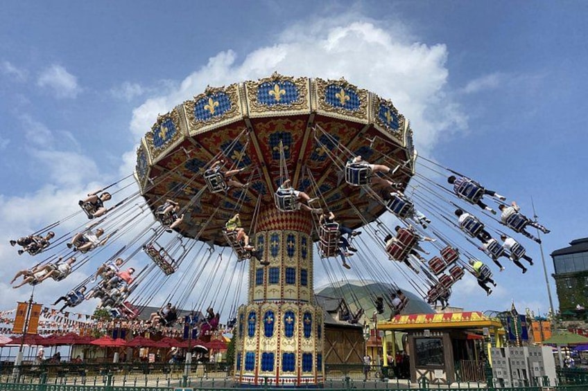 A large, ornate carousel with multiple horses and riders, set against a clear blue sky. 2
