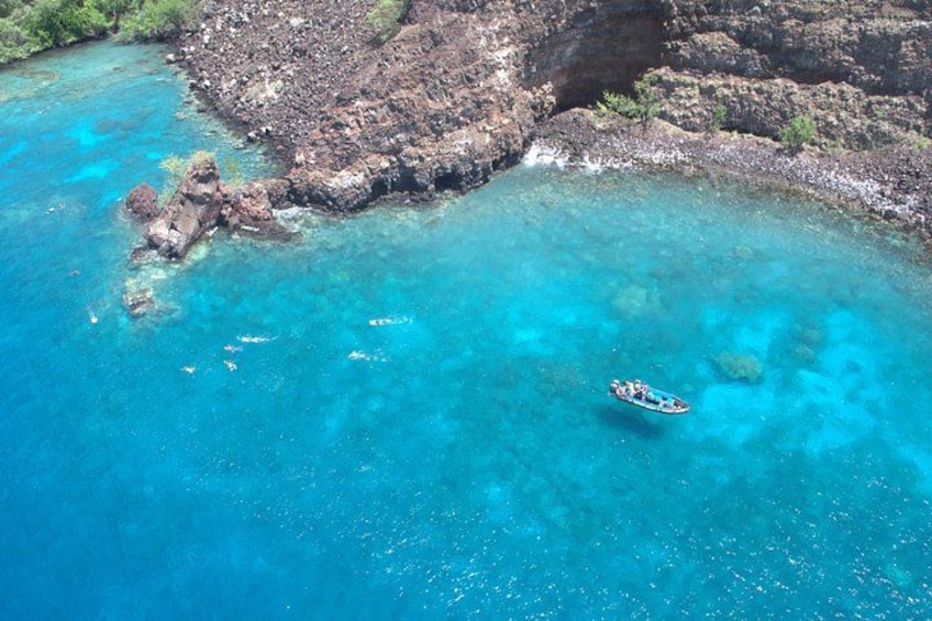 Une mer d’un bleu profond, avec une côte rocheuse et un petit bateau. 1