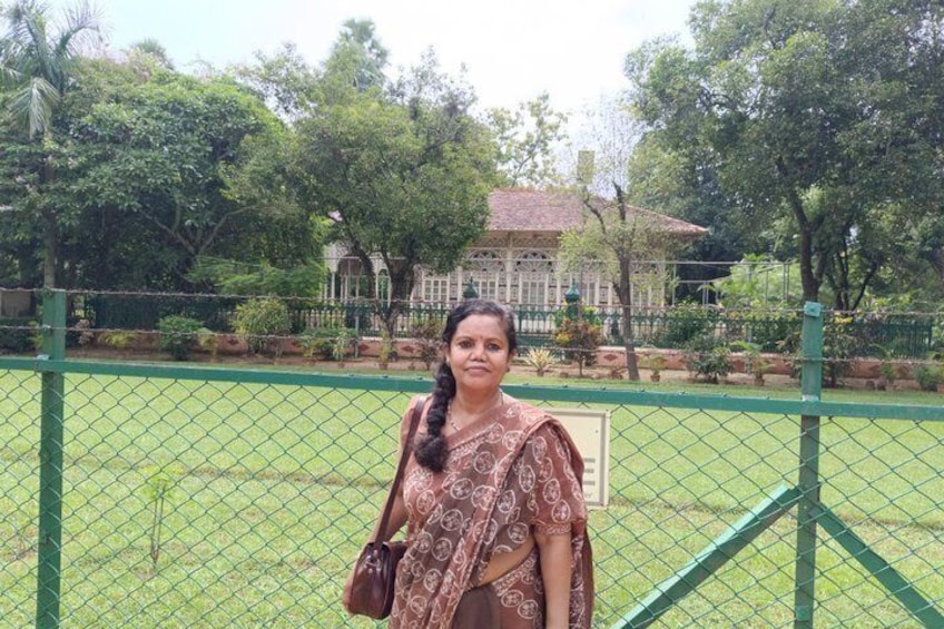 A person standing in front of a green fence with a building and trees in the background. 2