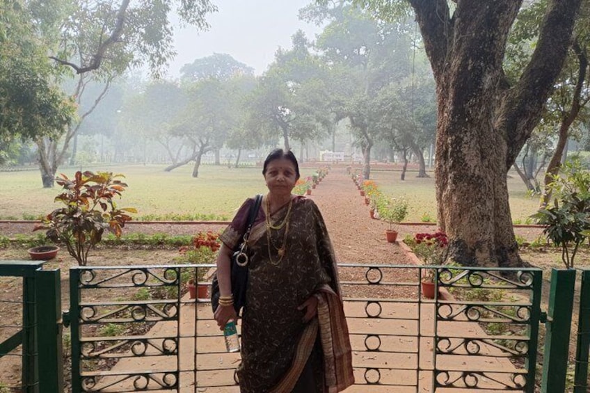 A person standing in a park with a pathway, trees, and potted plants. 5