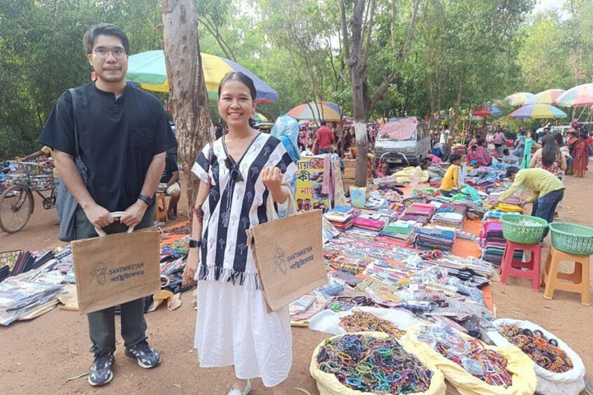 A market with people selling and buying goods, surrounded by trees and colorful umbrellas. 3