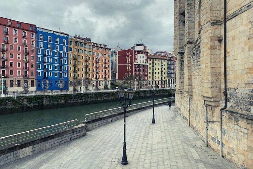 A riverside walkway with colorful buildings, a stone wall, and lampposts. 4