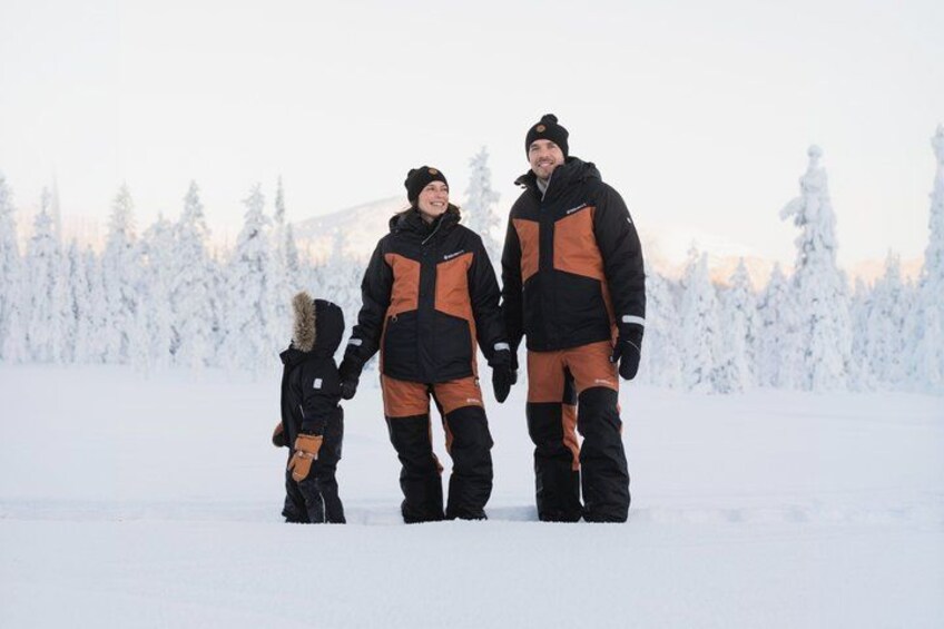 A family of three in winter clothing standing in a snowy landscape with trees in the background. 5