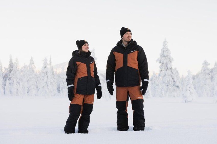 Two people standing in a snowy landscape with trees in the background. 1