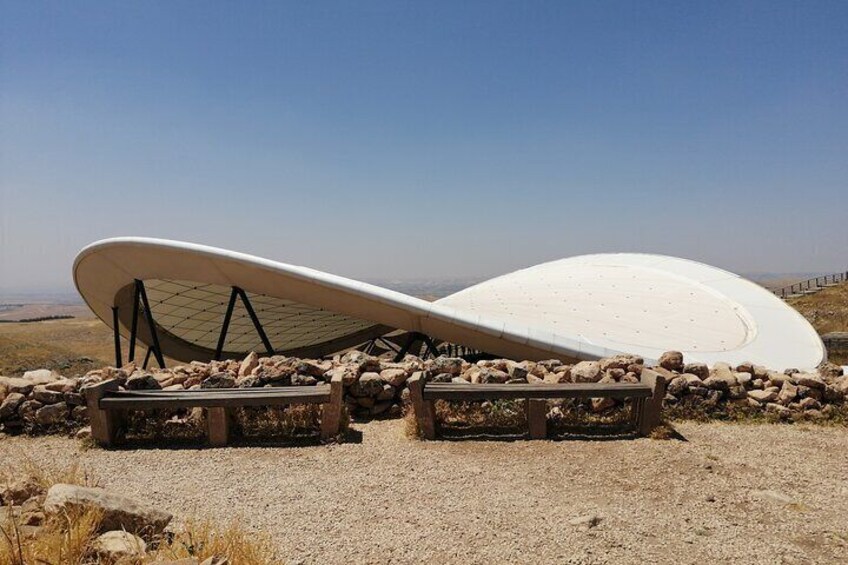 A modern architectural structure with a curved roof, surrounded by stone walls and gravel ground. 5