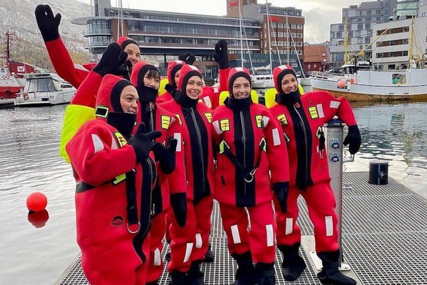 A group of people in red and black suits posing by a dock with boats and buildings in the background. 2