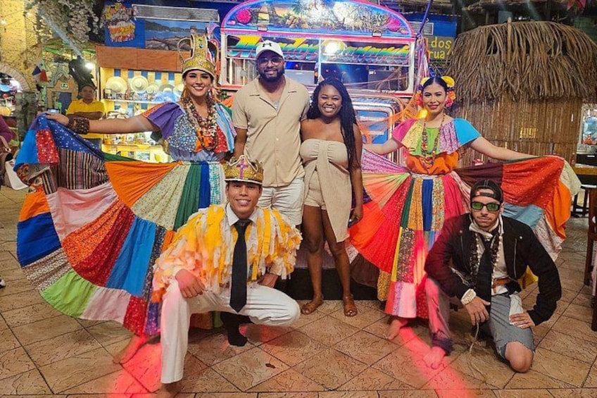 Un grupo de personas vestidas con atuendos tradicionales coloridos posando con un gran textil multicolor. 4