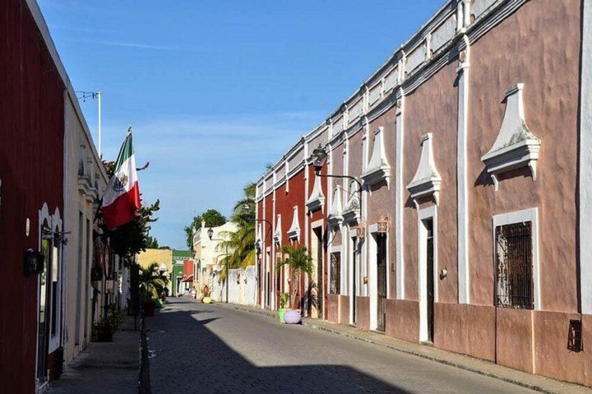 Una calle adoquinada flanqueada por edificios históricos, una bandera y un cielo azul despejado. 2