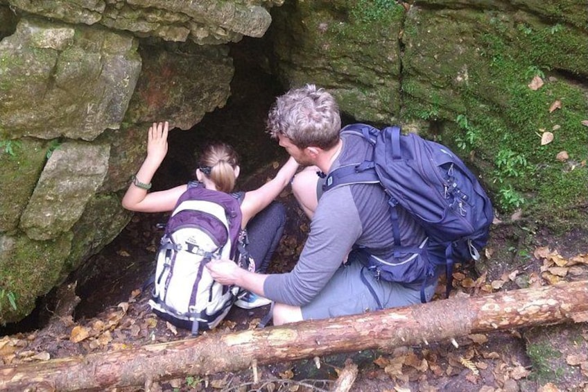 Two people hiking near a rocky cave entrance with backpacks. 1