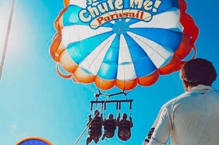 Une personne se tient sous un parachute, et on peut lire sur celui-ci : « Chute libre ! Parachutisme ». 1
