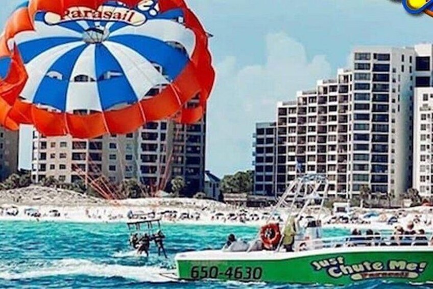 Un parachute ascensionnel avec une voile aux couleurs vives, un bateau à la coque verte et un paysage urbain avec de hauts immeubles en arrière-plan. 3