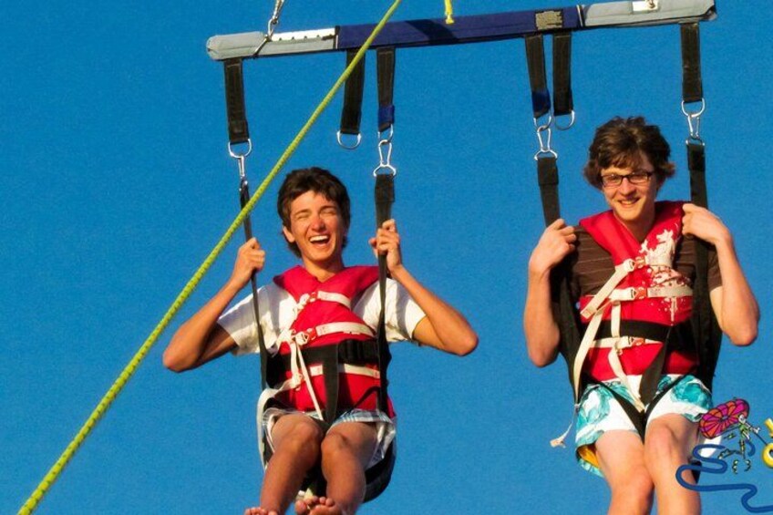 Dos personas en un columpio acuático, con chalecos salvavidas y agarrándose a las barras. 2