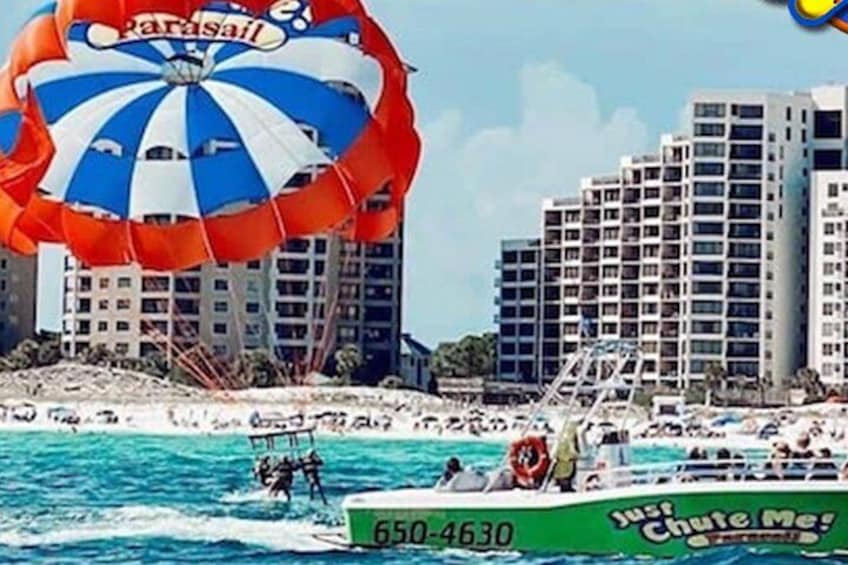 Un parasail con un dosel colorido, una lancha con casco verde y un paisaje urbano con edificios altos al fondo. 4