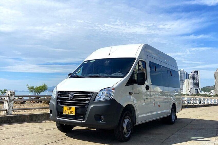 A white van parked on a paved area with a clear sky and distant buildings. 5