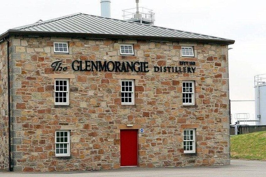 Un bâtiment en pierre avec une porte et des fenêtres rouges, portant l’inscription « The Glenmorangie Distillery ». 1