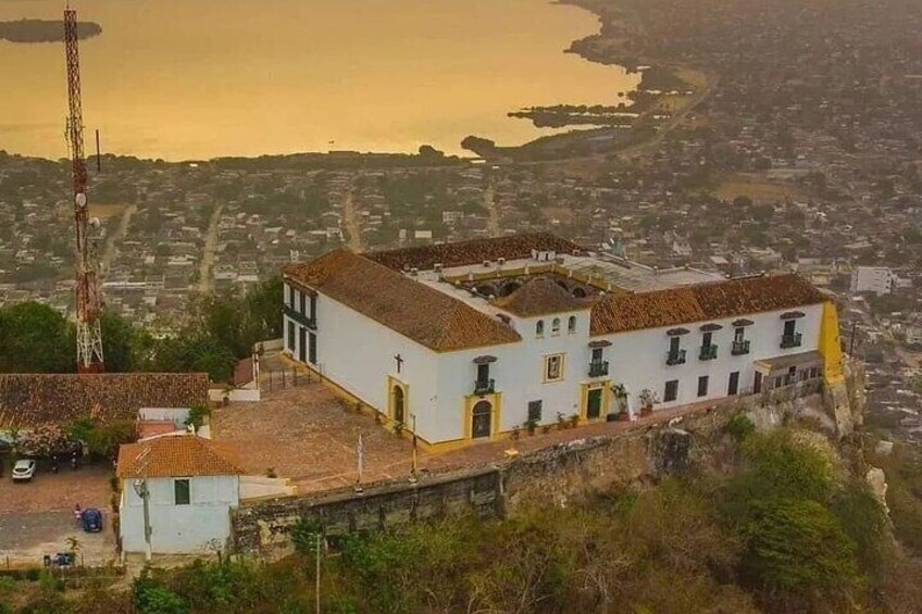 Un pueblo costero con una iglesia blanca destacada y techo rojo, una alta torre de comunicaciones, y vistas al mar y al paisaje urbano. 3