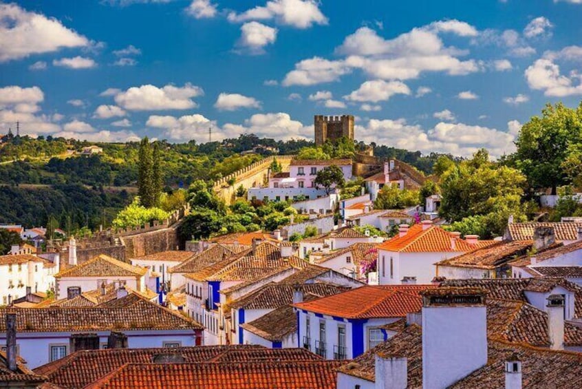A town with terracotta-roofed buildings, a prominent tower, and lush green hills in the background. 4