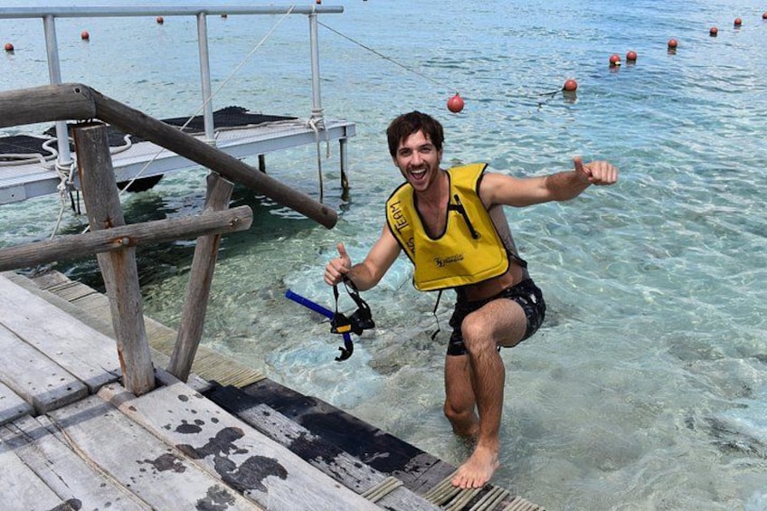 Una persona con chaleco salvavidas amarillo bajando de un muelle de madera a aguas transparentes. 3