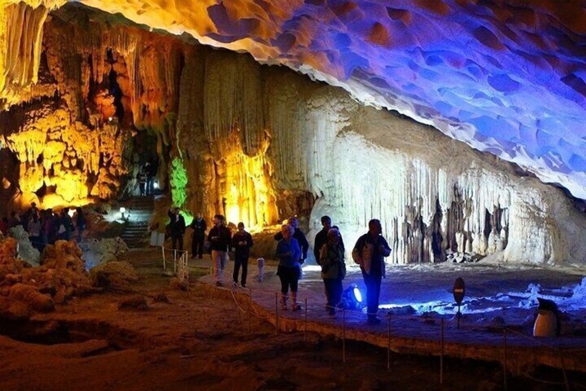 A cave with stalactites and stalagmites, illuminated by artificial lighting, with visitors exploring the formations. 2