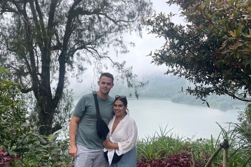 Two people standing by a lake with trees and fog in the background. 2