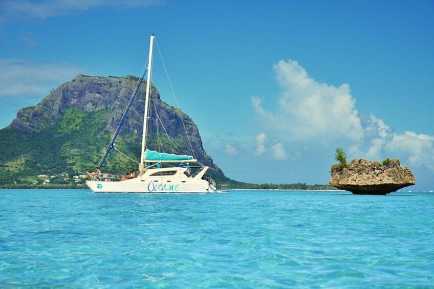 A sailboat named 'Ocean' on calm blue waters with a mountainous island in the background. 1