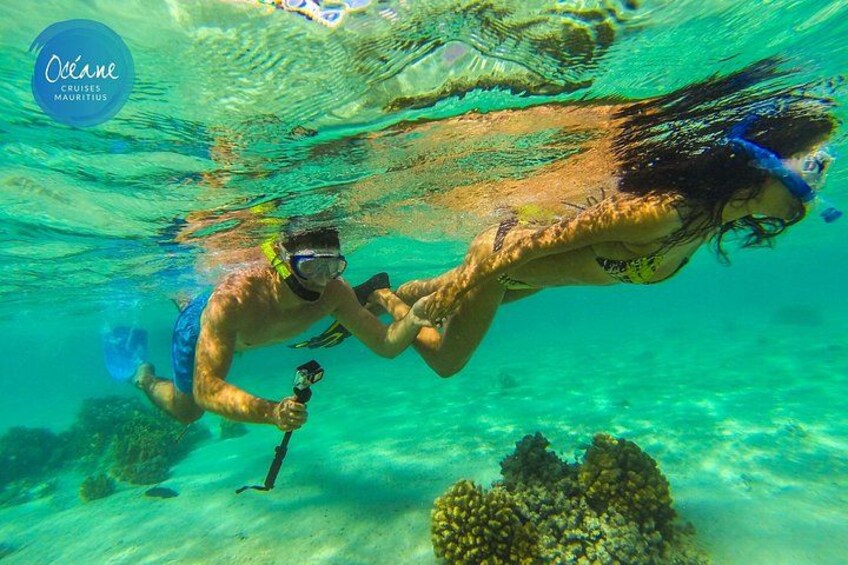 Two people snorkeling underwater with coral formations and a clear blue ocean. 2