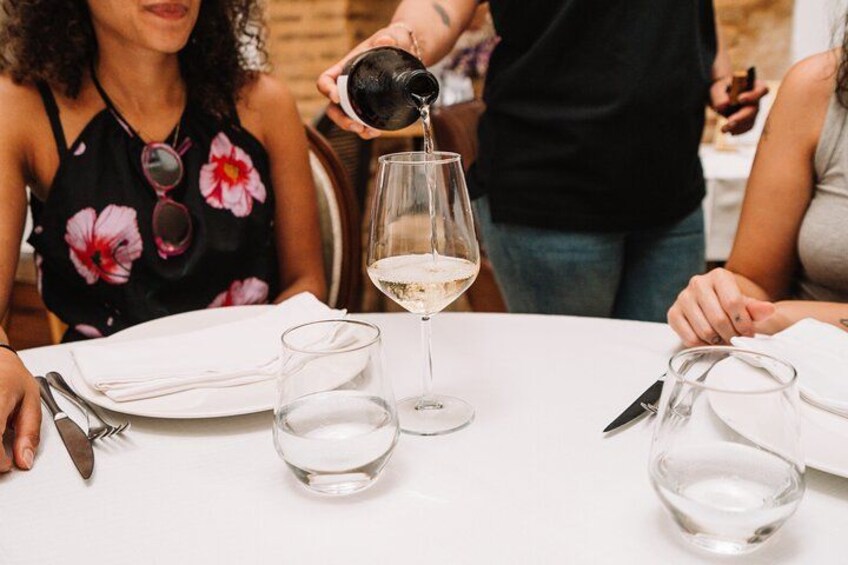 Une personne verse un liquide transparent dans un verre à vin, sur une table dressée pour le repas. 4
