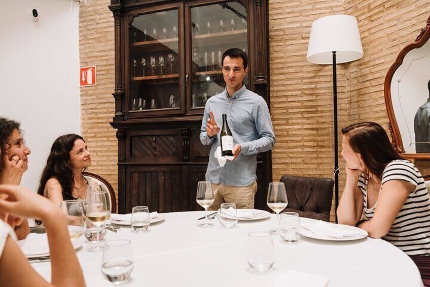 Un grupo de personas cenando en una mesa con un camarero sosteniendo una botella de vino. 3