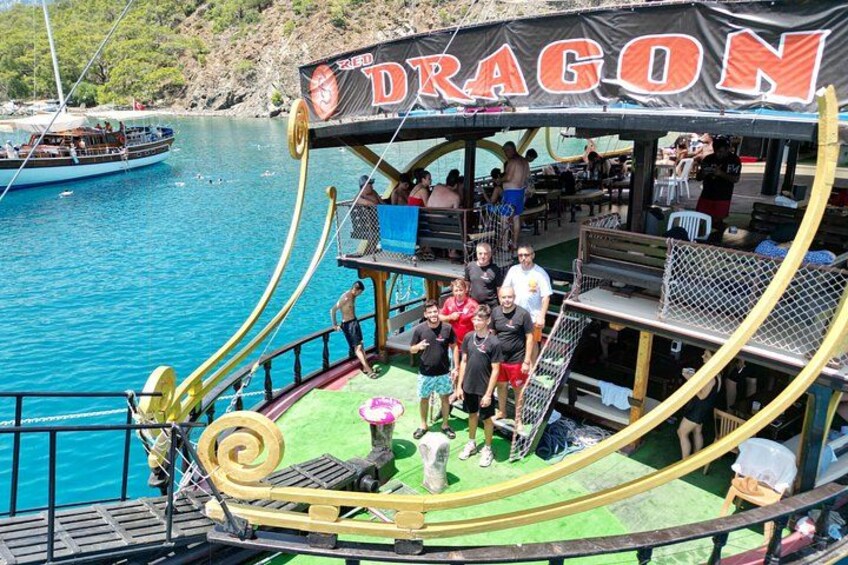 A boat named 'DRAGON' with people on deck, a green deck, and a blue water background. 3