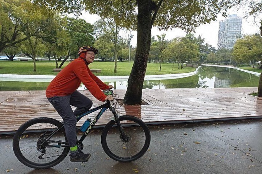 A person riding a bicycle on a wet pavement with trees and a body of water in the background. 4