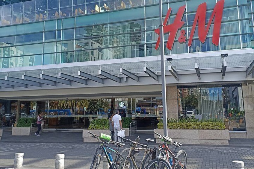 A modern building with a large red sign reading 'H&M'. There are bicycles parked in front and a person walking. 2