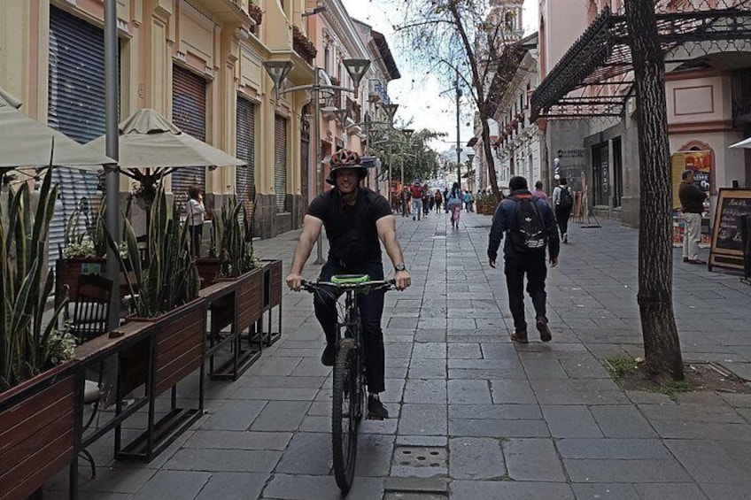 A person riding a bicycle on a paved street with benches and potted plants on the side. 5