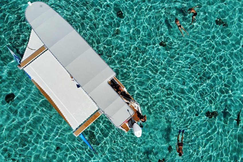 A white boat with a blue stripe on a turquoise water body with people swimming. 2