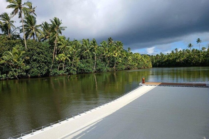 Un plan d’eau paisible, avec une jetée qui s’avance sur celui-ci, entouré d’une végétation tropicale luxuriante et de palmiers. 2